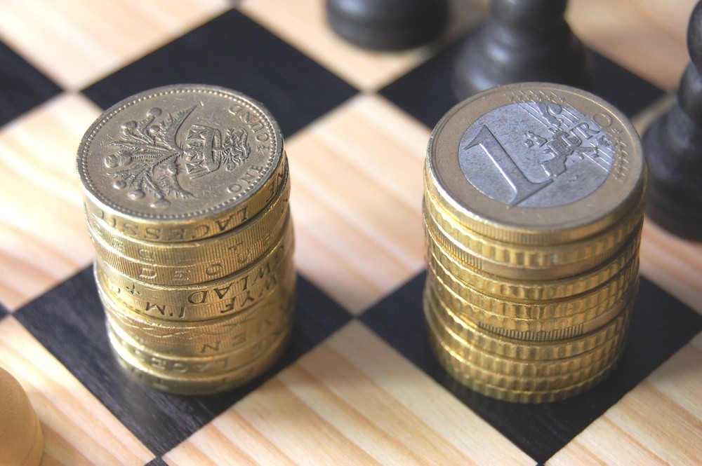 Wibest – EURGBP: A stack of British pound coins and a stack of euro coins over a chessboard. 